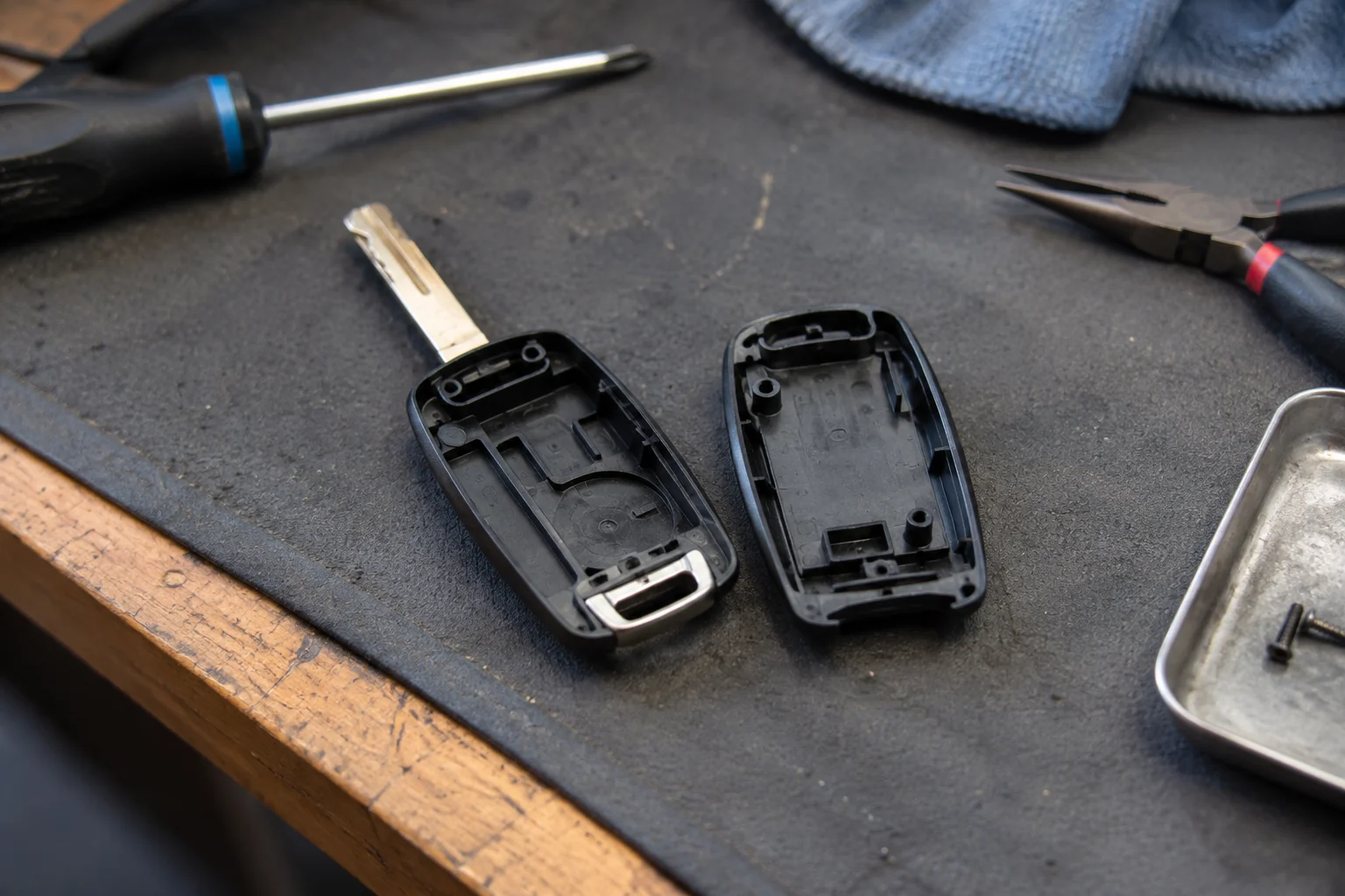 The open halves of an empty automotive key shell lie on a work mat, exposing their interiors.